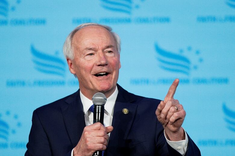 White haired man in blue suit speaking into a microphone