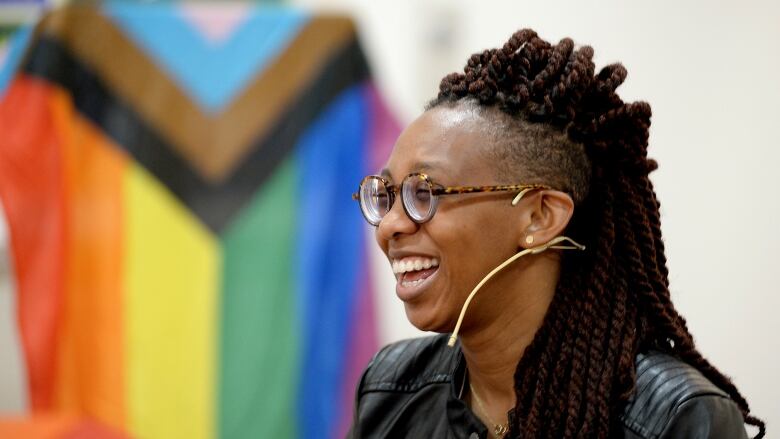 A person with an ear piece mic smiles as an LGBTQ flag is seen in the background.