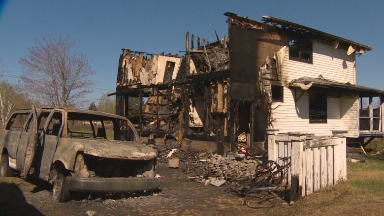 Blackened beams inside a shell of white siding. A charred van is in the foreground.