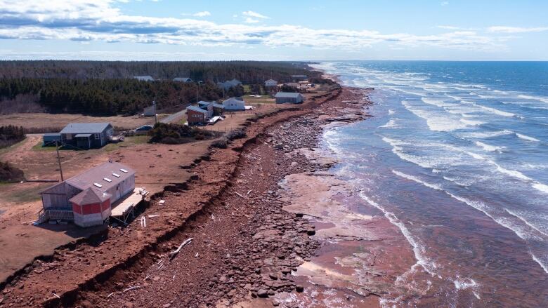 Drone shot of coastline with sand sucked off a rock beach and damage to nearby cottages.