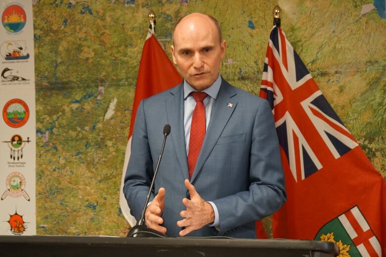 A man in a suit stands behind a podium and speaks into a microphone.