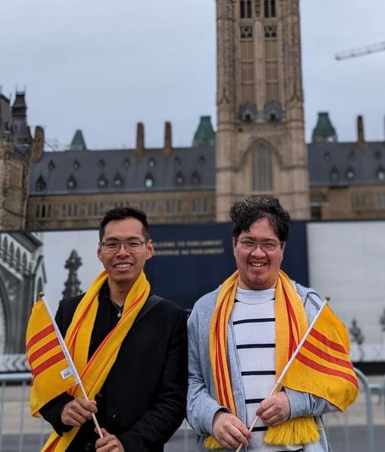 Two men with yellow and red flags in front of Canada's Parliament.