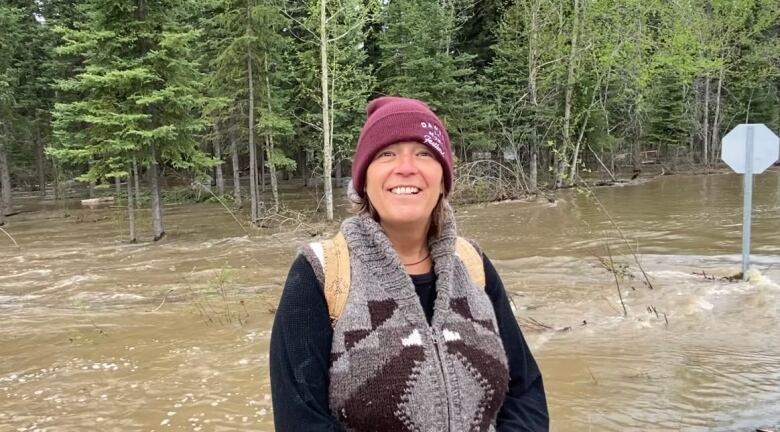 A woman stands in front of a flooded area of forest.