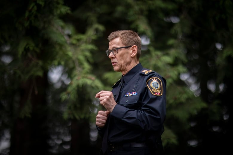 A white man wearing a police uniform gestures while speaking in a park.