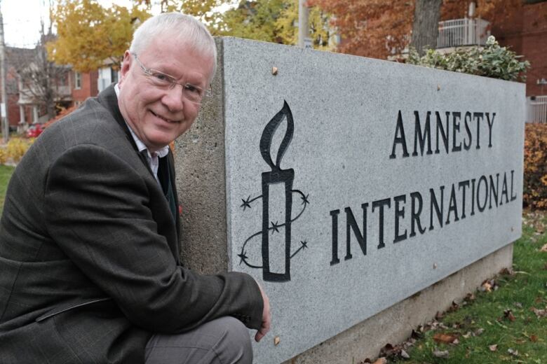 A man kneels next to an Amnesty International sign.