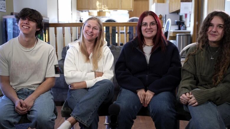 Four high school students side shoulder to shoulder in a kitchen, one is male, three are female