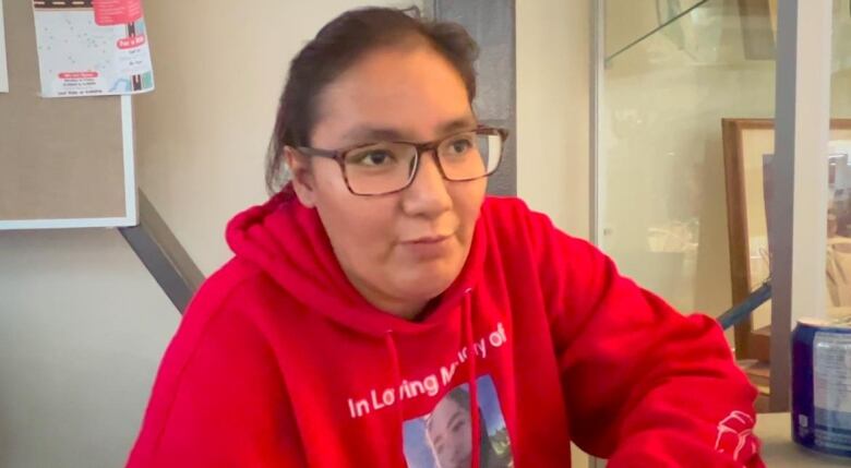 A woman wears a red sweatshirt and glasses while sitting.