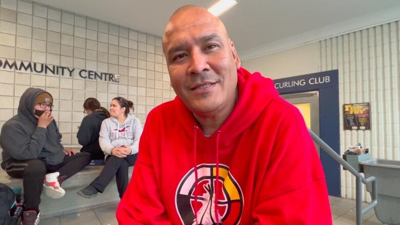 A man in a red hoodie with a medicine wheel looks at the camera.