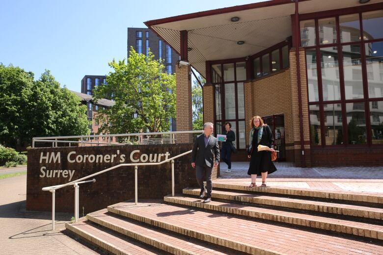 A man and two women walk down the steps of a large brick building. A sign nearby reads 