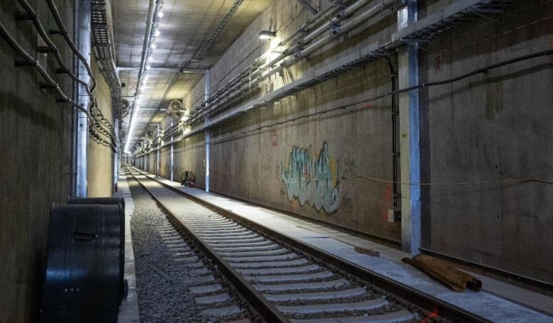 Tracks run through a tunnel, which has graffiti on one wall