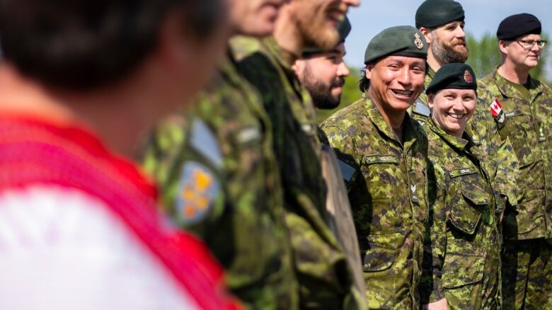 Military members stand in a line smiling.