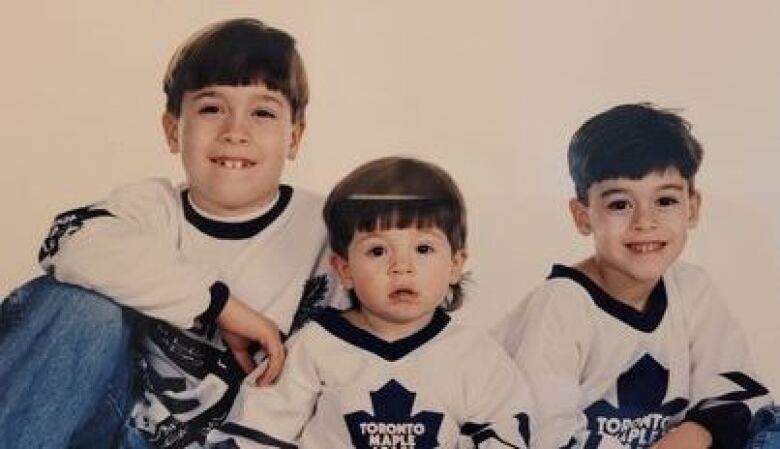 Three kids in Maple Leafs jerseys smile at the camera.