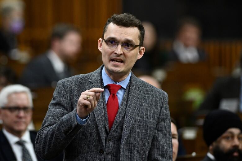 A man in a suit stands and gestures.