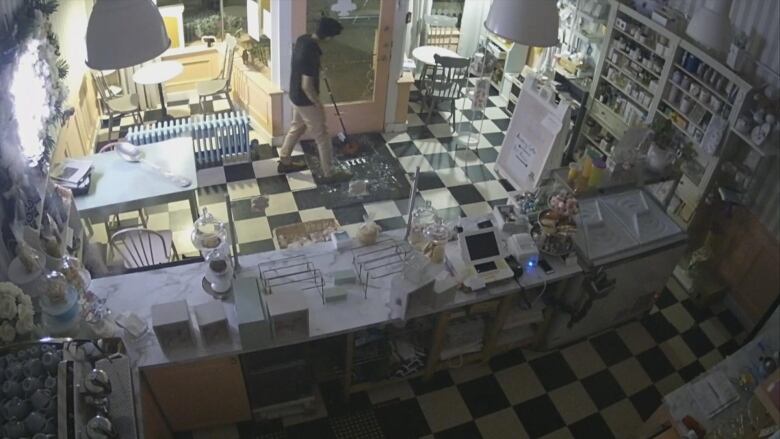 Security footage shows a man stands in a bakery at night time with a mop in hand surrounded by shattered glass. 