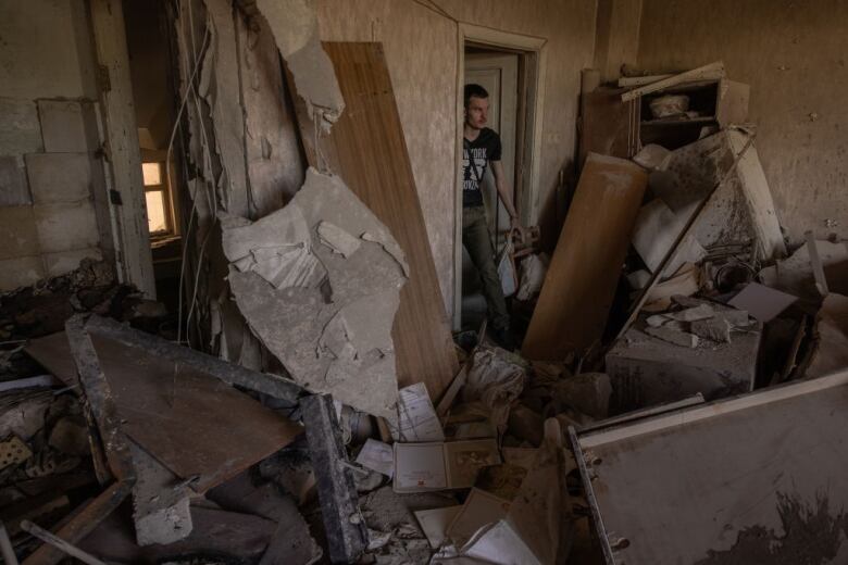 A man stands in the doorway of a damaged room filled with debris.