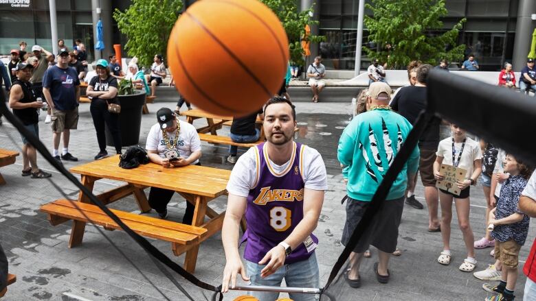 A man wearing a Lakers basketball jersey shoots a basketball into a small net. 