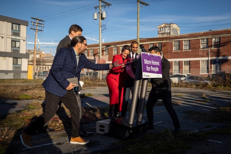 A tall podium tips at an outdoor news conference, as speakers rush to stop it from falling.