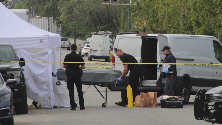 Police move a covered body on a stretcher into a van, surrounded by police tape.