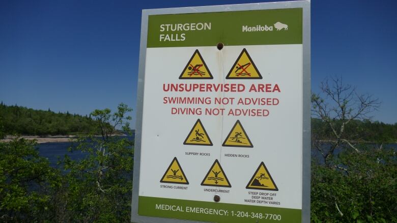 A sign telling people not to swim or dive into a nearby body of water is shown. It also advises of other dangers, including slippery rocks, hidden rocks, and strong currents.