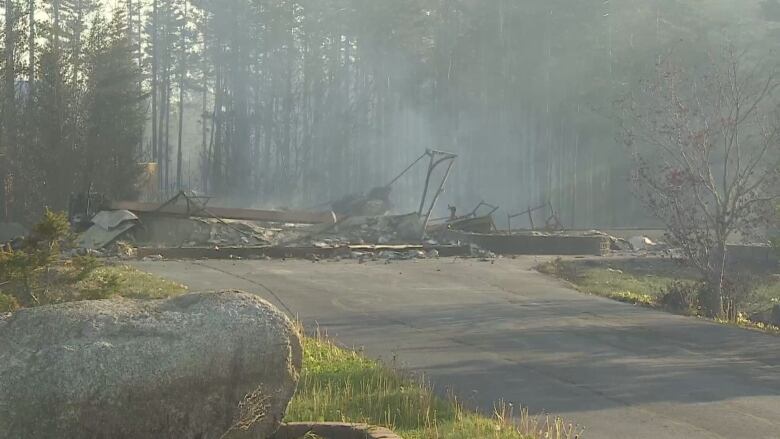 The smoking remains of a building with burnt trees visible in the background.