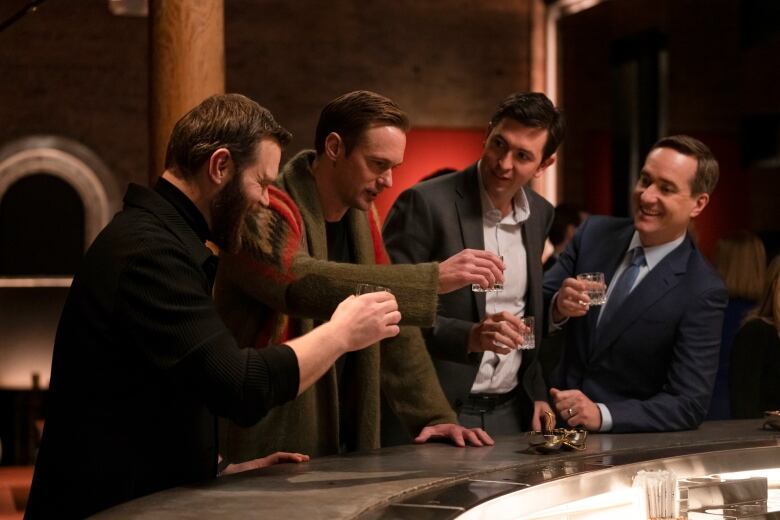 Four men raise their drinks at a bar.