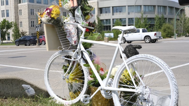 A memorial with a bike painted white is beside a post with flowers on an intersection. 