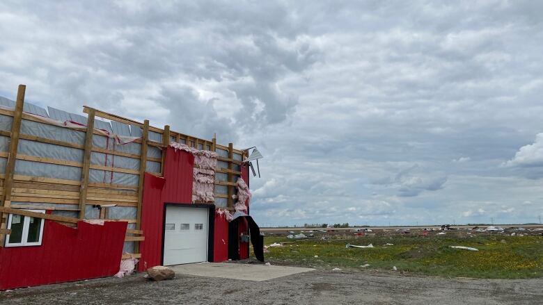 A red metal building torn to its studs with debris splayed in a field behind it