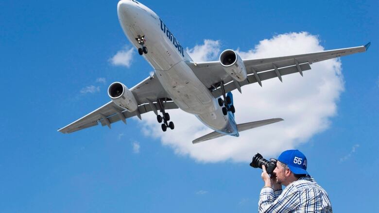 A man takes photos of a passenger jet coming in to land.