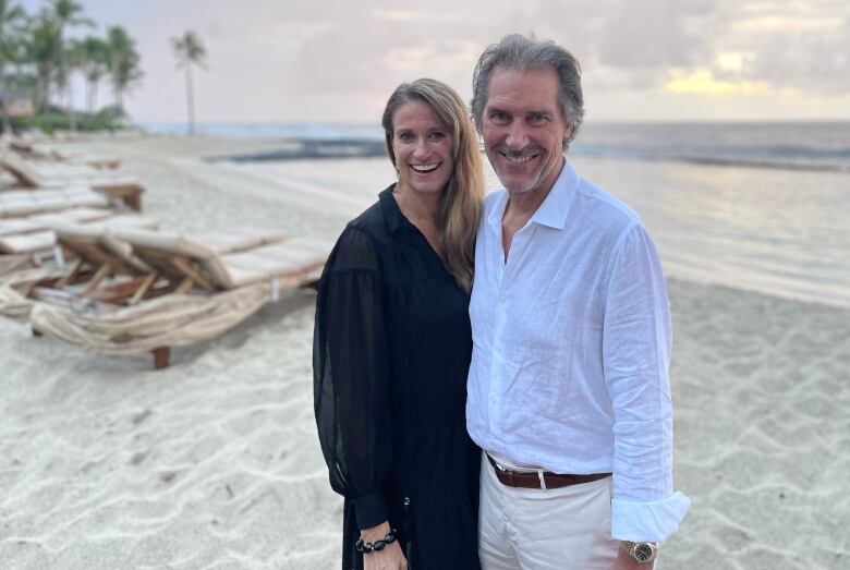 A woman smiles next to a white man while on a beach.