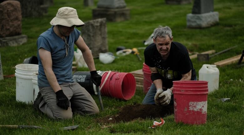 Two men kneel as they carefully remove dirt from a hole with their hands.