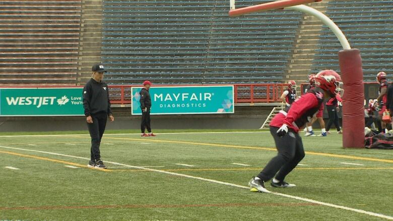 A woman watches as a football player sprints to a cone.