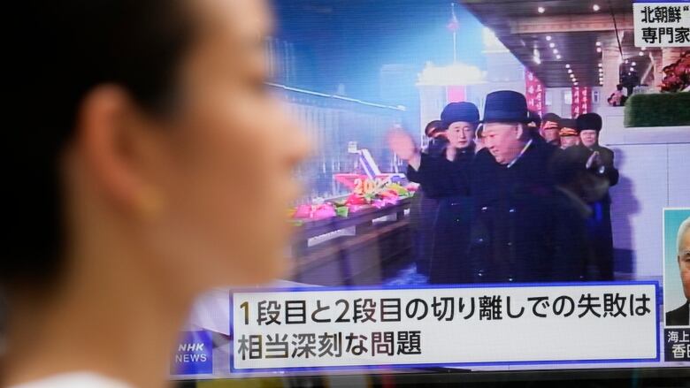 A person passes in front of a television screen showing North Korean leader Kim Jong-un waving and a banner with Japanese text.