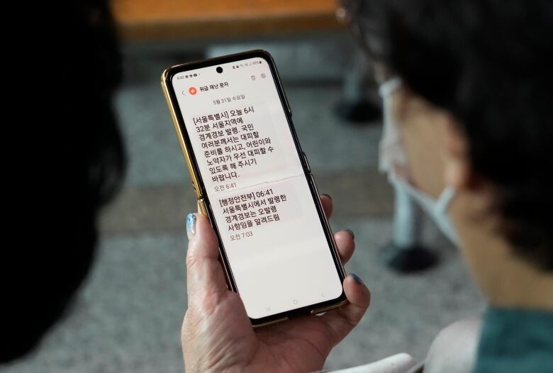 A person looks at a mobile phone with Korean text.