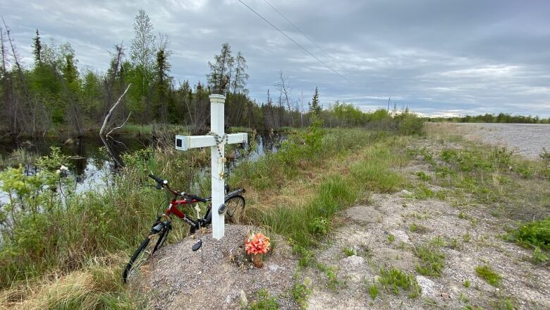 White cross on grass with beads on it, bike. 