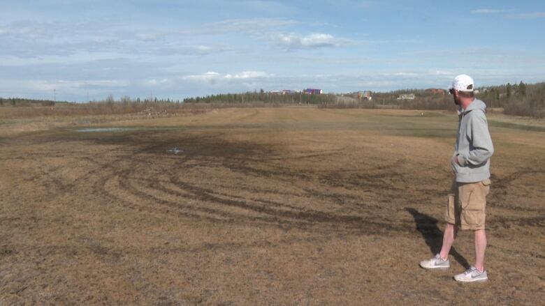 A man stands on a muddy, grassy field.