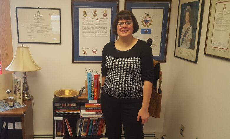 A woman stands in a room with official documents framed on the wall.