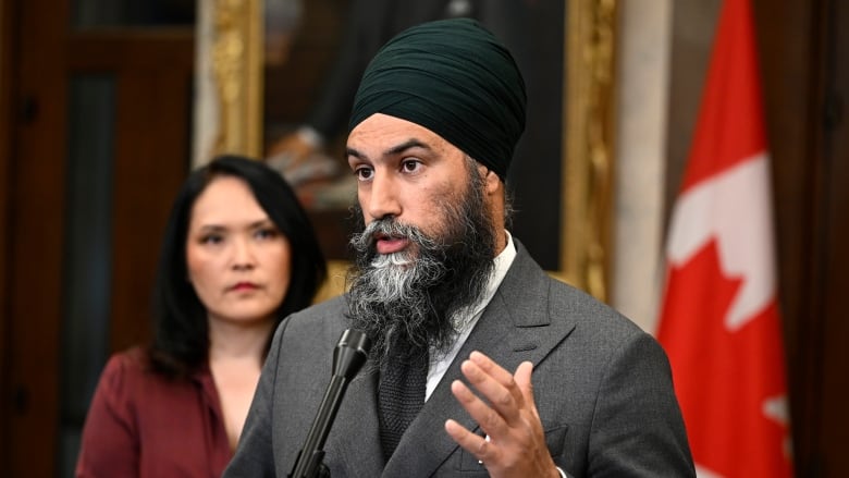 A man in a gray suit answers reporters' questions outside the House of Commons.