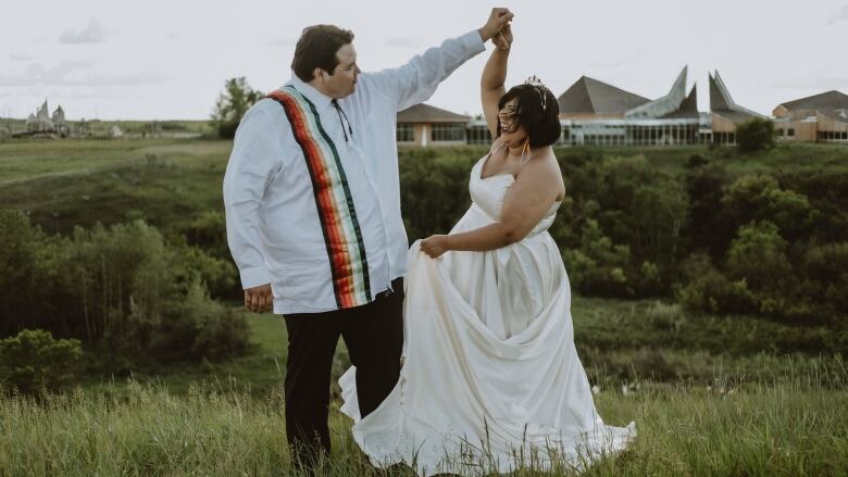 A man and woman in wedding attire dance in a field. 