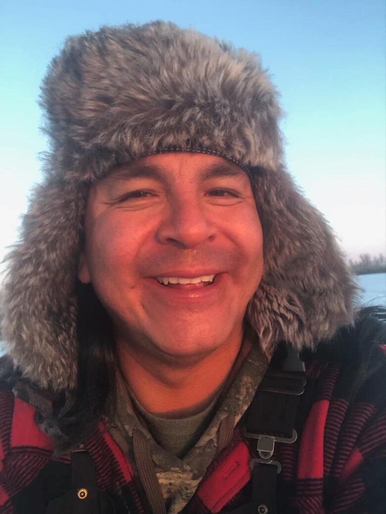 A man in a winter hat and plaid jacket smiles.