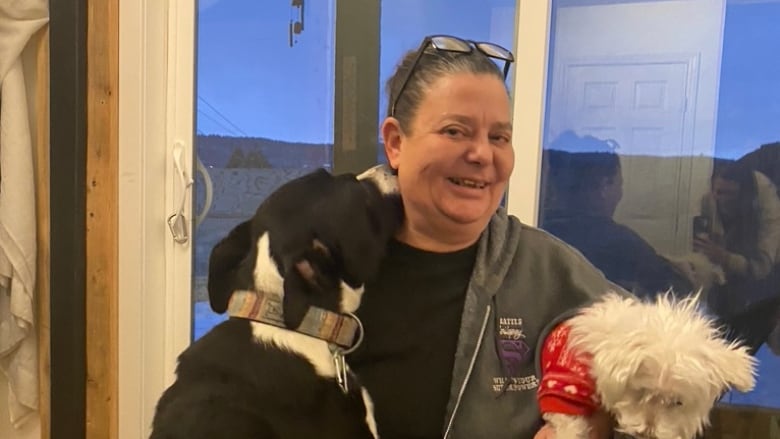 A woman is pictured smiling, holding two dogs. 