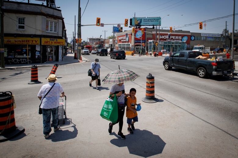 Pedestrians cross an intersection while taking shade from the sun under an umbrella.