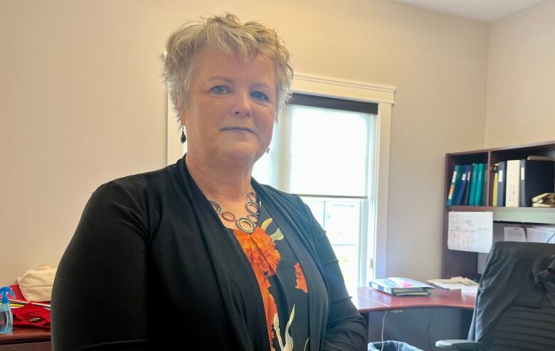 A woman stands smiling at the camera in an office.