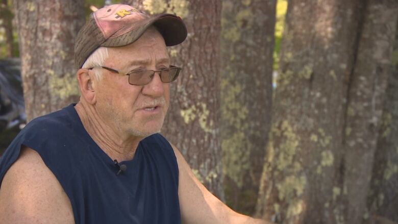 A man is seen wearing transition lenses, a ball cap and a navy sleeveless shirt.