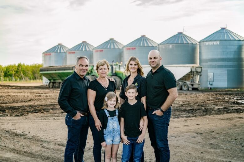 A three-generation family stands in front of some grain bins.