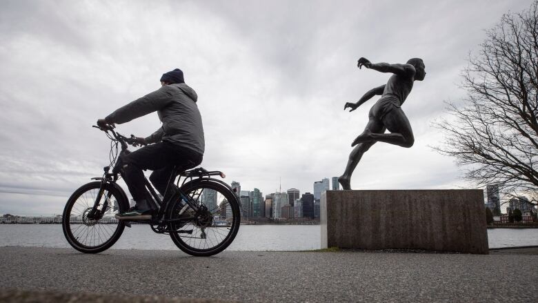 Cyclist rides an e-bike along seawall near statue in Vancouver