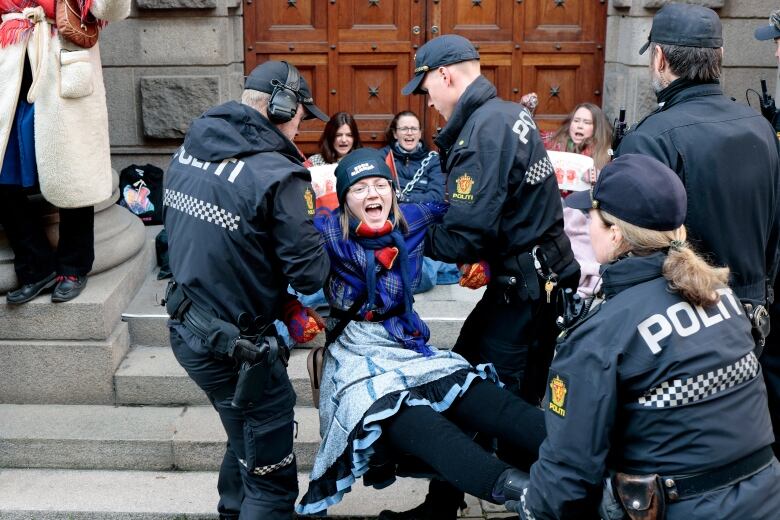 A young woman in a warm hat is carried away by police. 