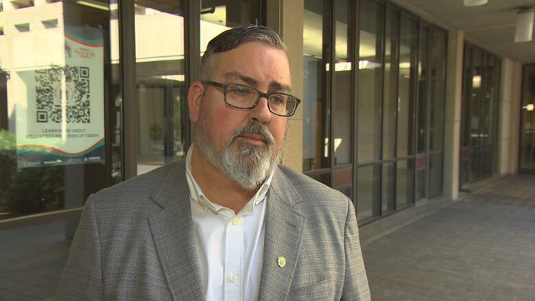 A white man with a goatee speaks to a reporter. 