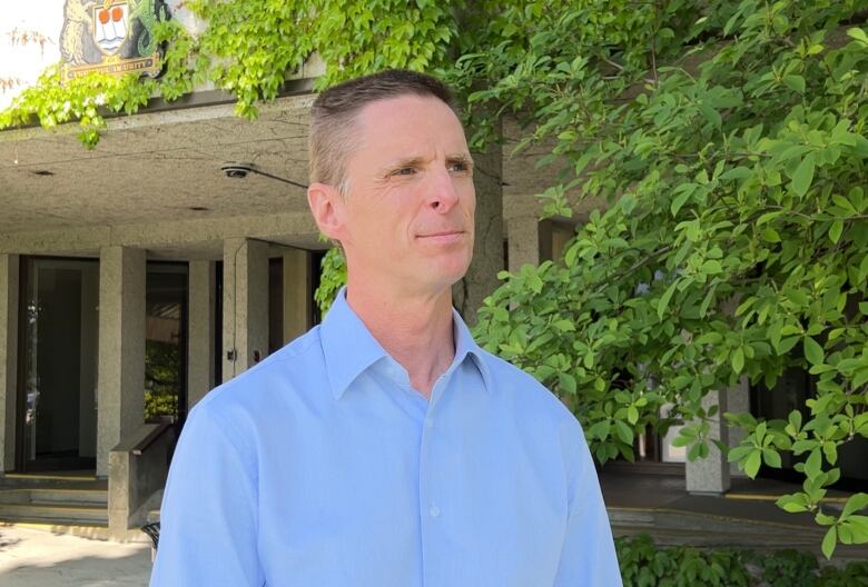 A man in a blue shirt stands in front of a building.