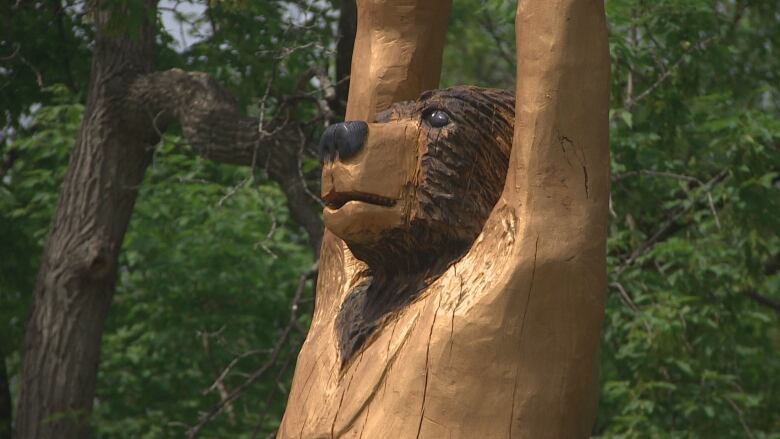 A wooden carving of a bear stands in front of trees.