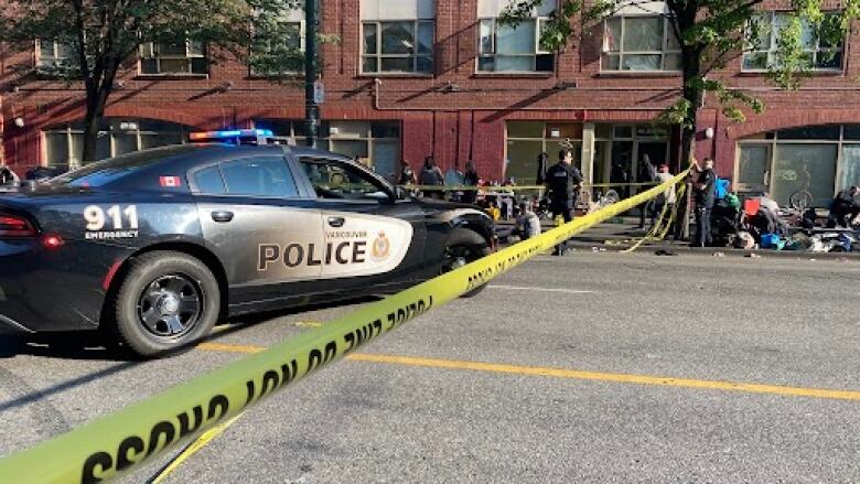 Police tape crosses a street with a police car parked behind it.